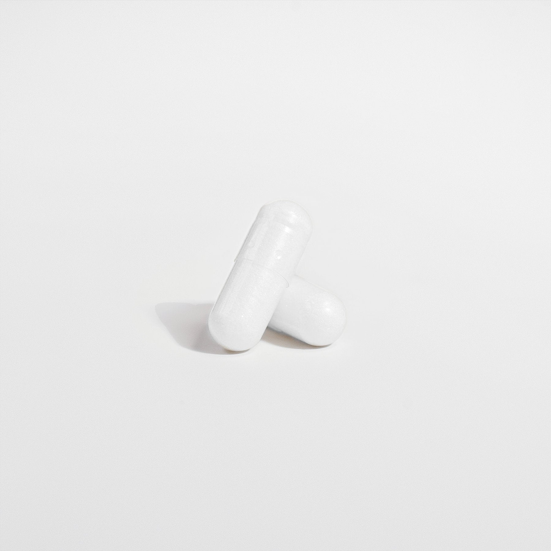 Two capsules of 111 & COMPANY BONE & HEART SUPPORT, a product by 111 & Company for bone health, sit on a light gray surface. One is horizontal and partially overlaps the vertically positioned one. Shadows suggest overhead lighting, enhancing the focus on the capsules.