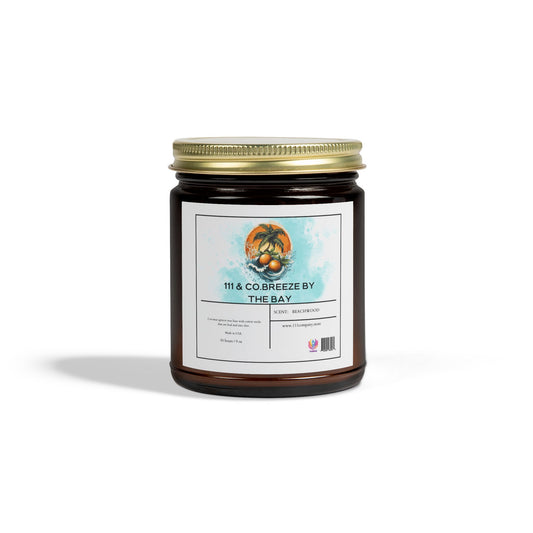 The 111 & Company Breeze by the Bay amber jar candle, crafted with coconut apricot wax and featuring a beachwood scent, includes a white-labeled seashell and palm tree design on a blue watercolor background with a gold lid.