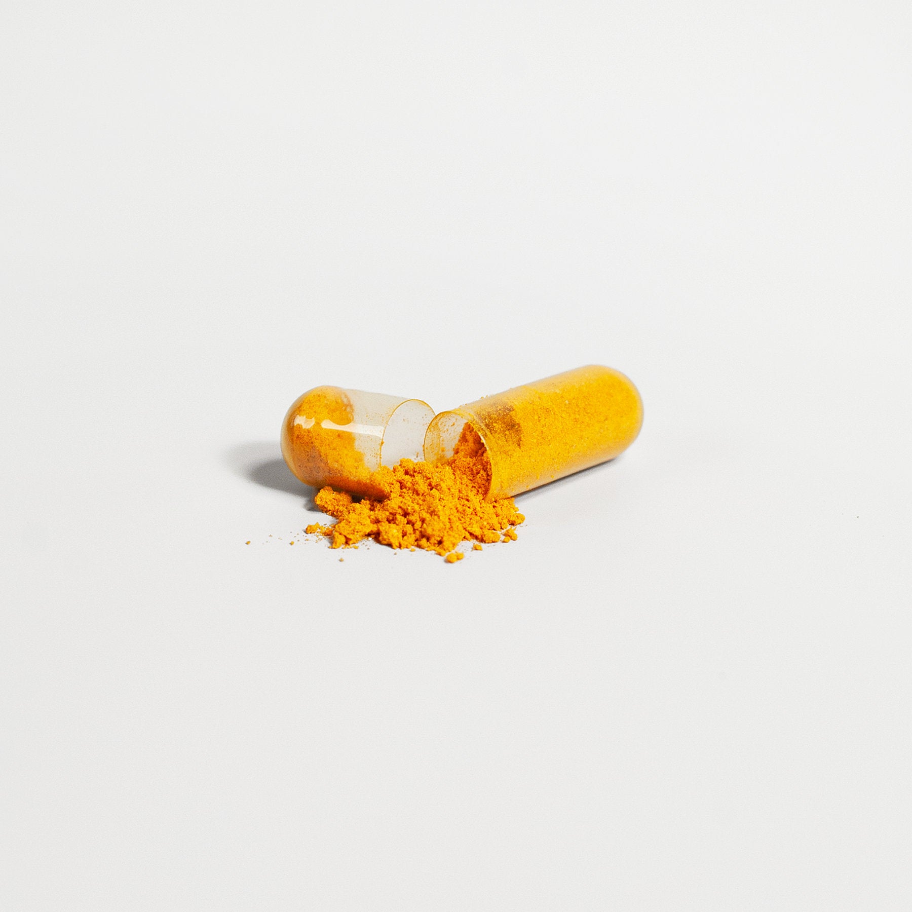 A transparent capsule of 111 & COMPANY CoQ10 UBIQUINONE 200 MG spills open on a white background. Bright orange powder, reminiscent of turmeric, scatters around the capsule, showcasing a vibrant contrast with the white surface and evoking thoughts of energy production from natures bounty.