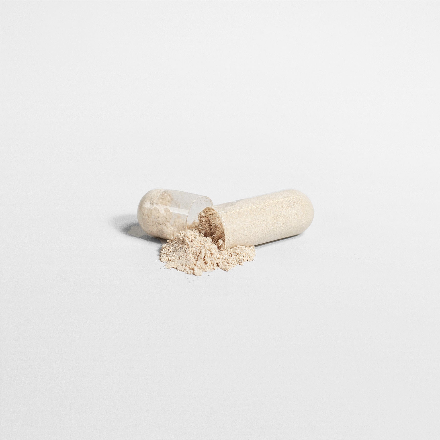 The 111 & Company COMPLETE MULTIVITAMIN capsule is open, spilling its fine beige powder onto a simple white surface. The capsule halves nestle the nutrient-rich multivitamin, enhanced with natural antioxidants.