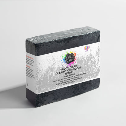 The 111 & Company Dark Delight Charcoal Soap is a black rectangular bar with a white label adorned with colorful watercolor splotches, highlighting its natural, handmade benefits. Displayed on a plain white surface, the soap proudly showcases its deep cleansing properties.