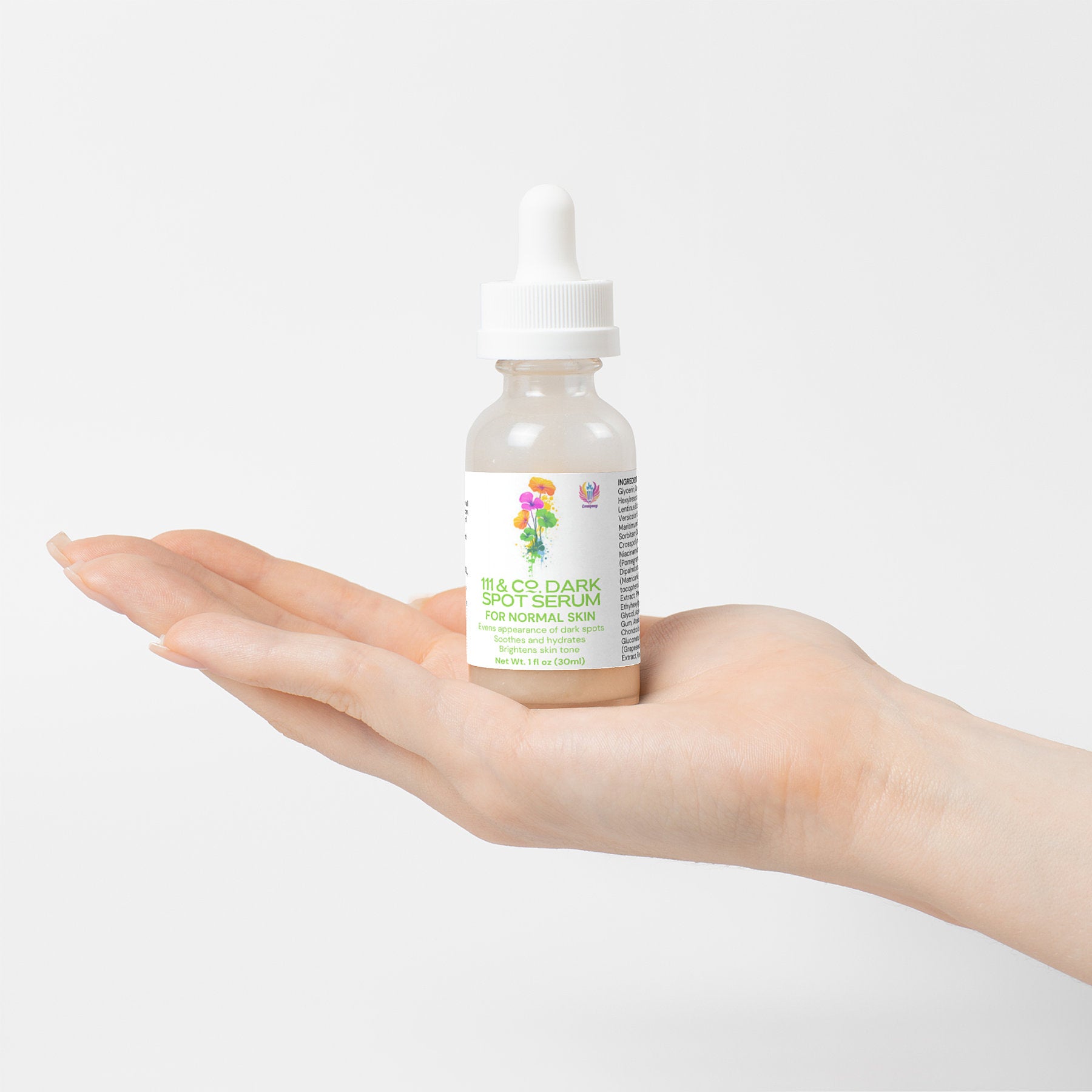 A hand holds a small bottle of 111 & Company Dark Spot Serum for Normal Skin, designed to reduce dark spots and even skin tone. The dropper cap complements the labels colorful floral graphics, making the product stand out elegantly against the plain white background.