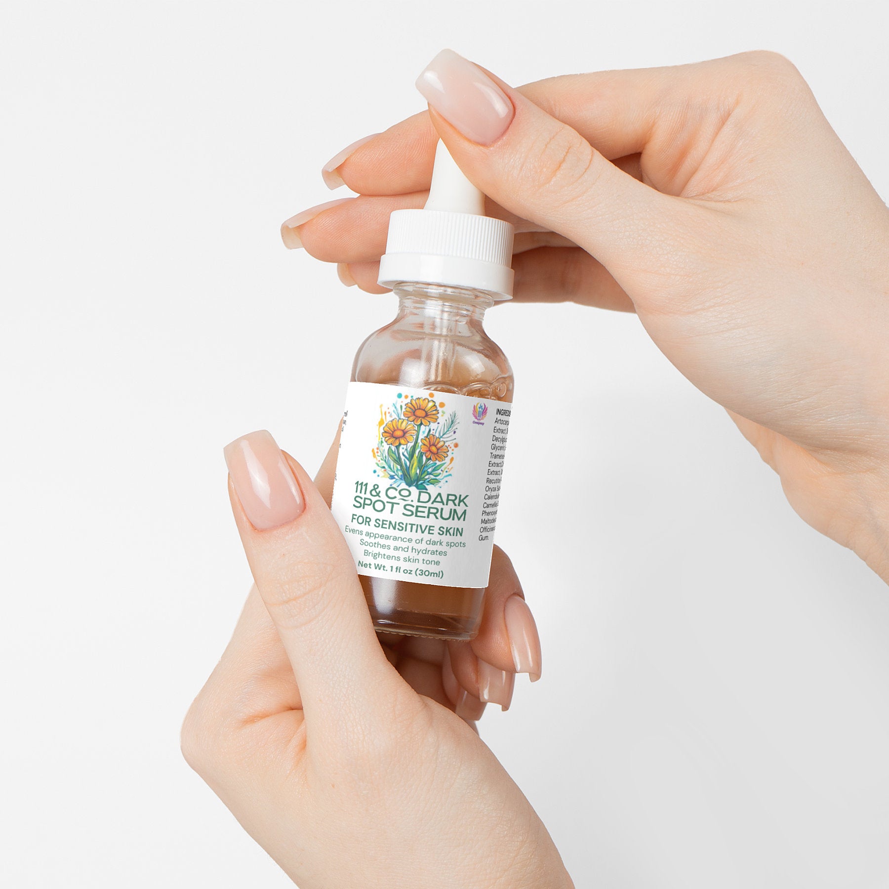 A close-up shows manicured hands holding a glass bottle of 111 & Company Dark Spot Serum for Sensitive Skin. The dropper cap and colorful floral label accentuate its natural ingredients, with For Sensitive Skin prominently displayed. A plain white backdrop highlights its purity.