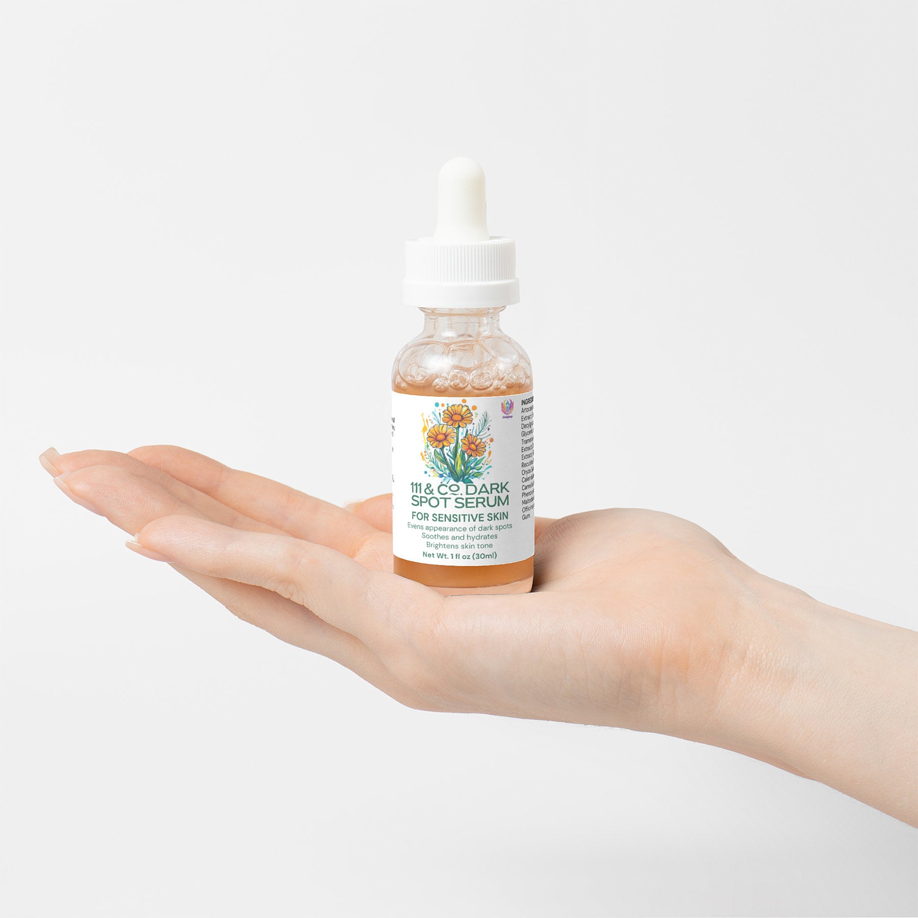 A hand holds a bottle of 111 & Company Dark Spot Serum for Sensitive Skin, crafted with natural ingredients. The glass bottle boasts a dropper and a floral illustrated label. The clear serum contrasts the plain white backdrop, emphasizing purity.