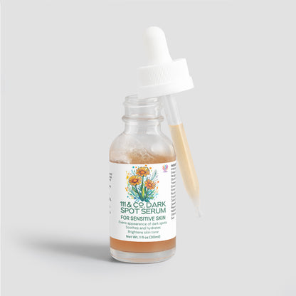 A glass dropper bottle displays 111 & Company Dark Spot Serum for Sensitive Skin with floral illustrations. The opened dropper, resting on the rim, holds a beige liquid. Made from natural ingredients, this 1 fl oz (30 ml) serum is crafted to even skin tone and brighten.