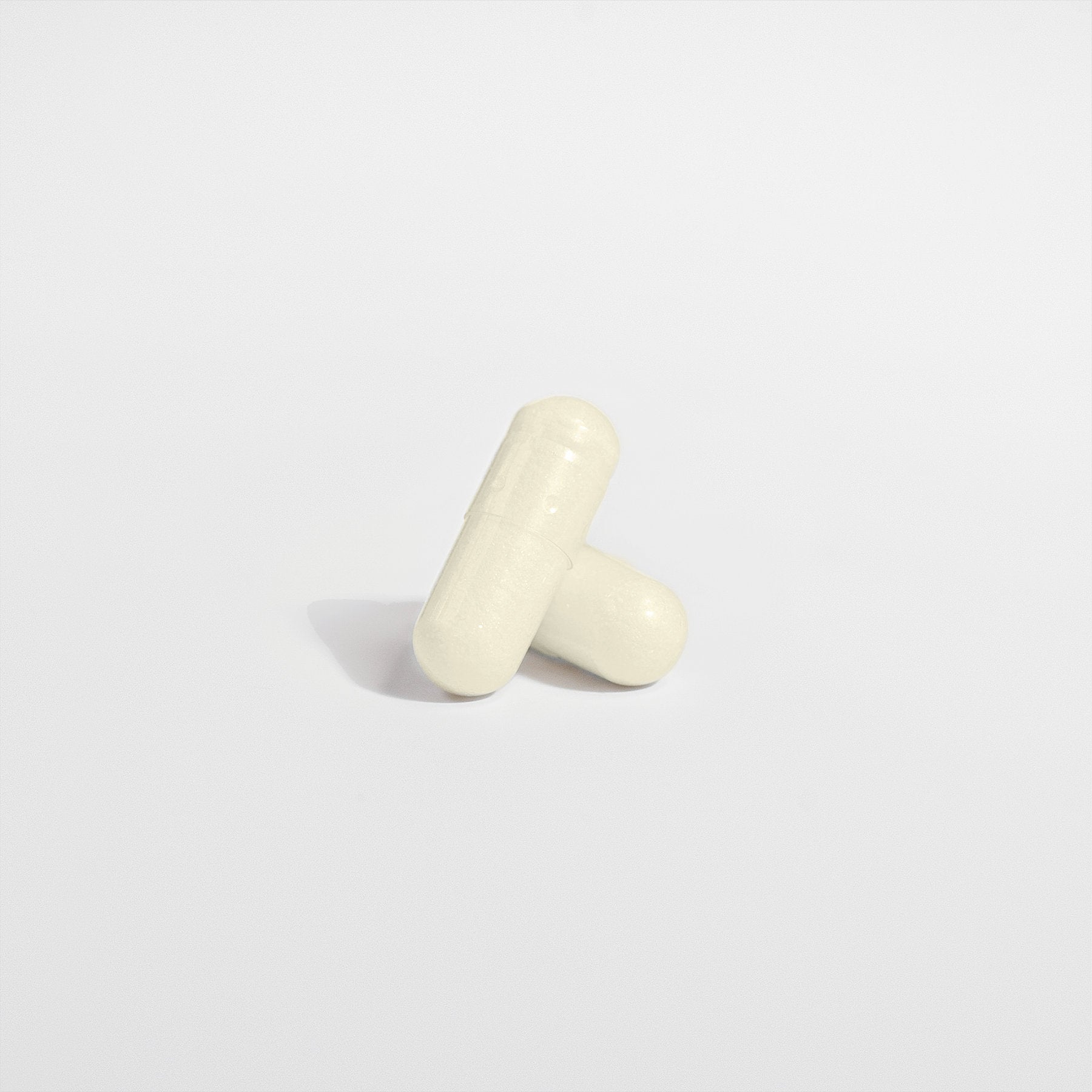 The minimalist image shows two white capsules of 111 & COMPANY DIGESTIVE ENZYME PRO BLEND by 111 & Company on a plain background. One leans diagonally against the other, both casting soft shadows, highlighting their smooth textures and seam lines for a simple, clean look.