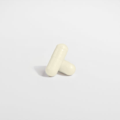 The minimalist image shows two white capsules of 111 & COMPANY DIGESTIVE ENZYME PRO BLEND by 111 & Company on a plain background. One leans diagonally against the other, both casting soft shadows, highlighting their smooth textures and seam lines for a simple, clean look.