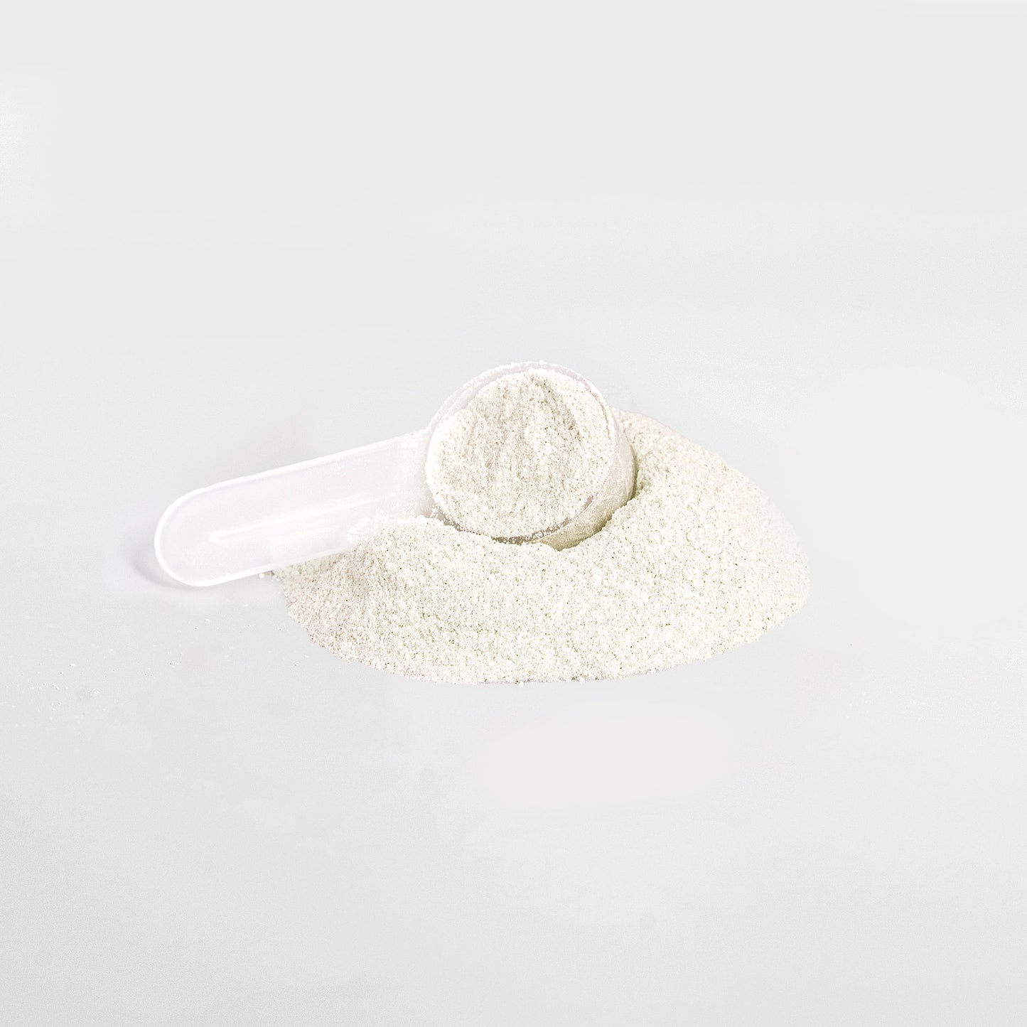 A plastic scoop partially buried in a heap of 111 & Company Energy Powder (Yuzu Flavor) on a plain white background, filled with fine, light powder, promising balanced energy in every measure.