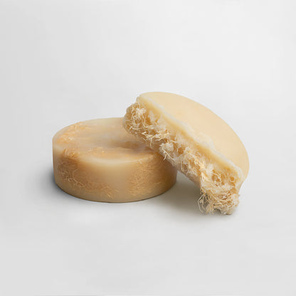 Two round bars of 111 & COMPANY EXFOLIATING LUFFA BAR soap are shown on a plain white backdrop. One lies flat, and the other leans against it, featuring netted textures similar to a loofah for exfoliation, embodying natural skincare.