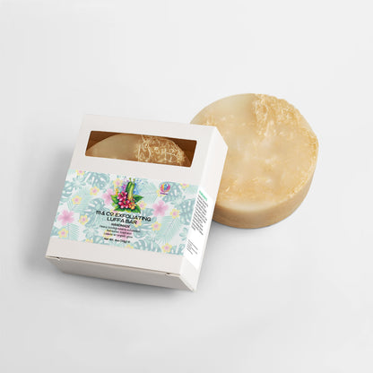 A round, tan soap bar lies next to an open white box with a transparent window. The box features colorful tropical designs and reads 111 & COMPANY EXFOLIATING LUFFA BAR, highlighting its biodegradable exfoliation benefits. Embedded luffa pieces are visible on the soaps surface.