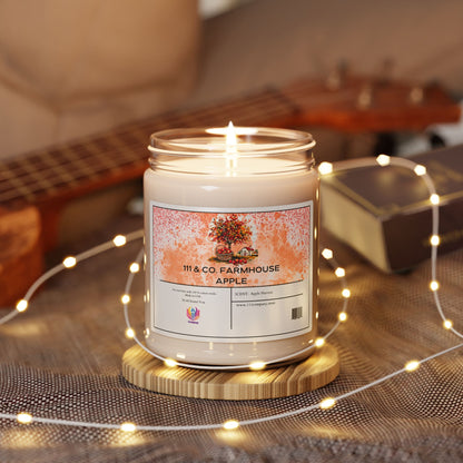 A lit 111 & Company Farmhouse Apple Harvest soy candle in a glass jar rests on a wooden coaster. Surrounded by yellow fairy lights, a closed book, and a blurred ukulele, it evokes autumn with the scent of apples and flowers.