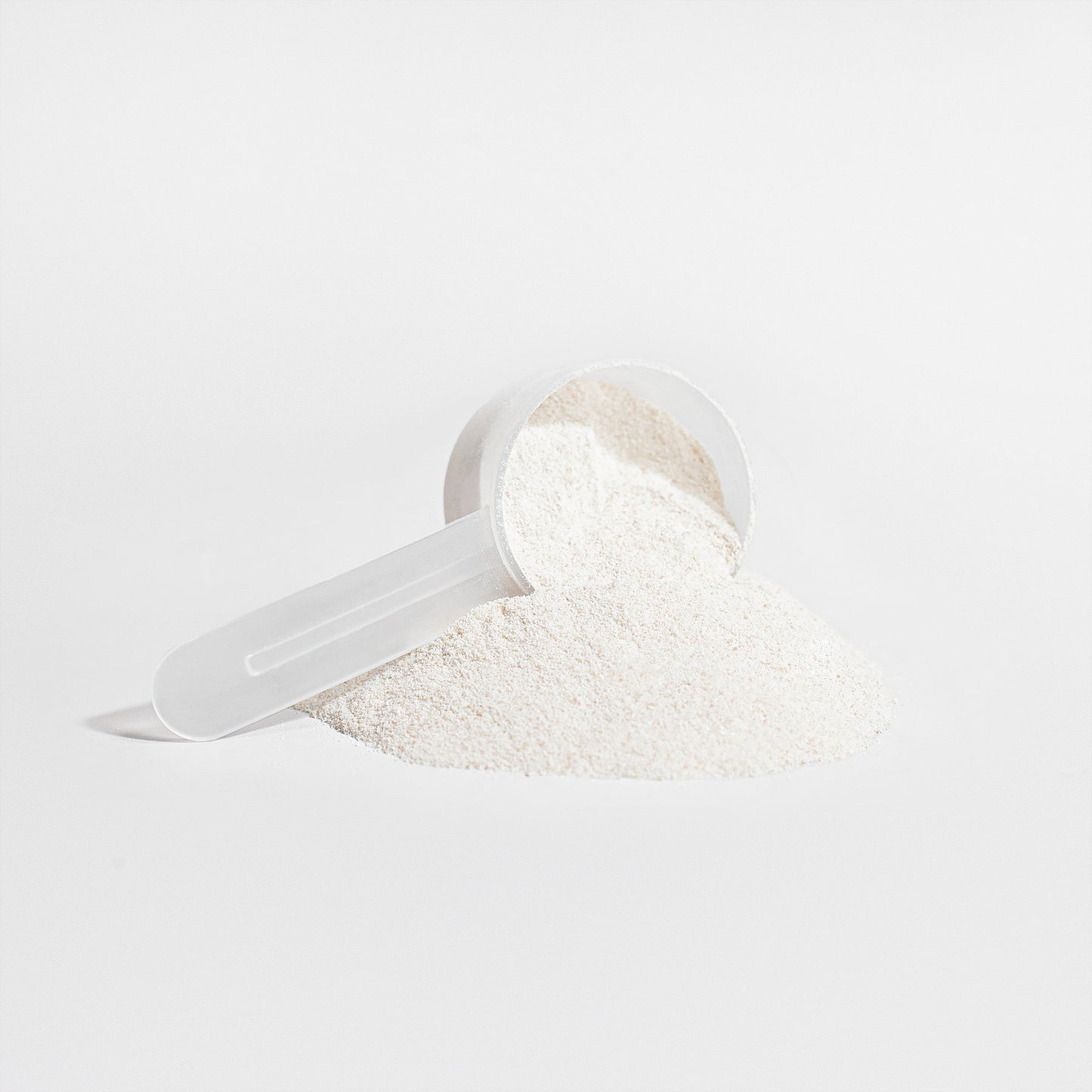 A white plastic scoop filled with fine, white hydrolyzed collagen peptides from 111 & COMPANY GRASS-FED COLLAGEN CREAMER (VANILLA) rests sideways on a white background. Some powder spills out, forming a neat mound, conveying a minimalist and clean aesthetic.