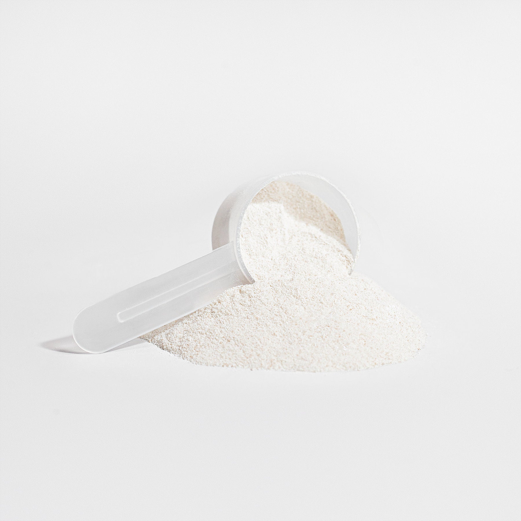 A white plastic scoop filled with fine, white hydrolyzed collagen peptides from 111 & COMPANY GRASS-FED COLLAGEN CREAMER (VANILLA) rests sideways on a white background. Some powder spills out, forming a neat mound, conveying a minimalist and clean aesthetic.