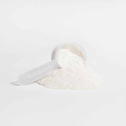 A white plastic scoop filled with fine, white hydrolyzed collagen peptides from 111 & COMPANY GRASS-FED COLLAGEN CREAMER (VANILLA) rests sideways on a white background. Some powder spills out, forming a neat mound, conveying a minimalist and clean aesthetic.