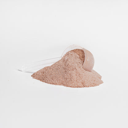 A clear plastic scoop of 111 & Company Grass-Fed Collagen Peptides Powder (Chocolate) is tipped over on a white surface, with some powder spilled in front, forming a small pile. The entirely white background emphasizes the texture and color of this rejuvenating supplement.