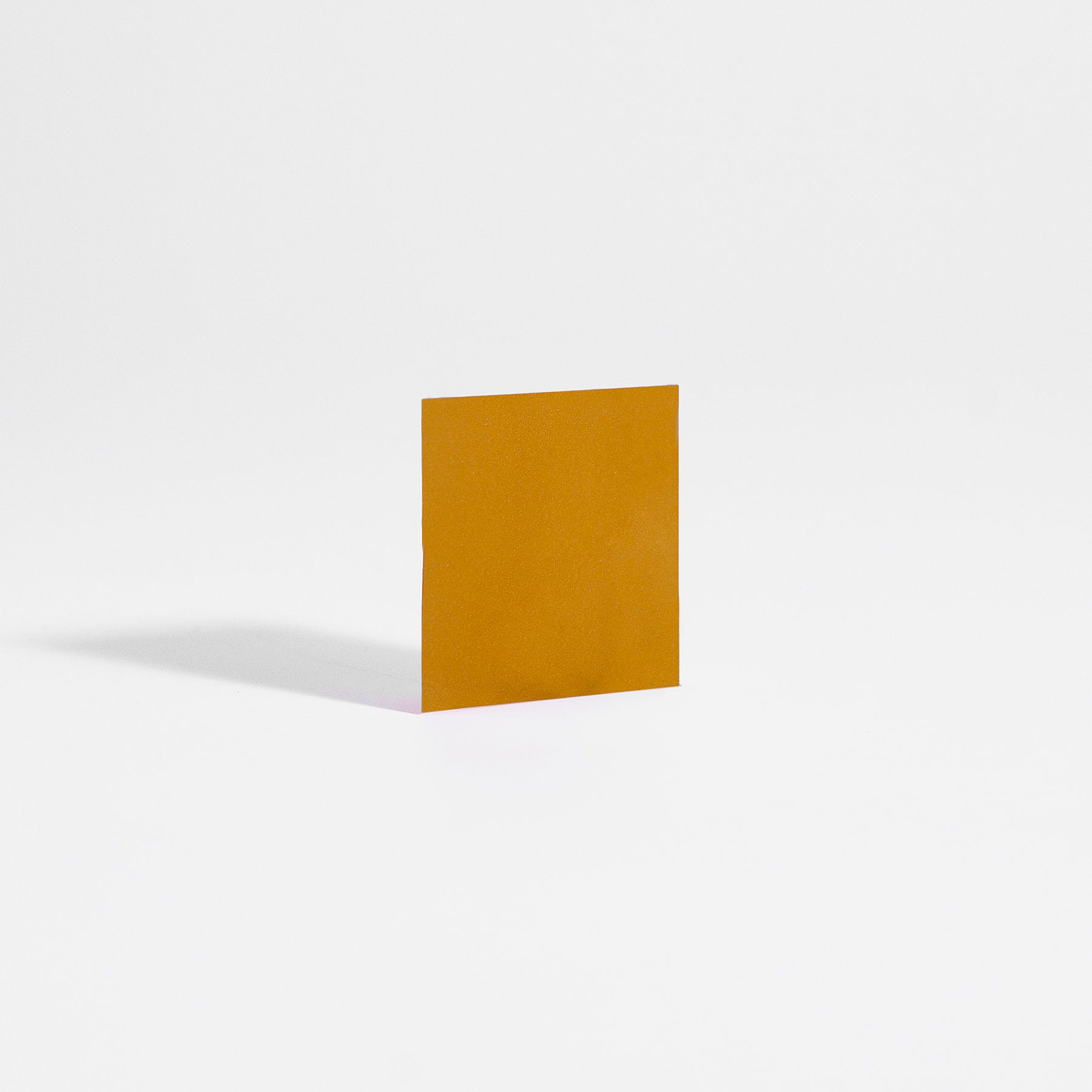 A square of mango and orange Hangover Strips from 111 & Company stands upright on a smooth white surface, casting a faint shadow to its left. Reminiscent of Ayurvedic practices, the strips vivid packaging is highlighted against the clean, minimalist background.