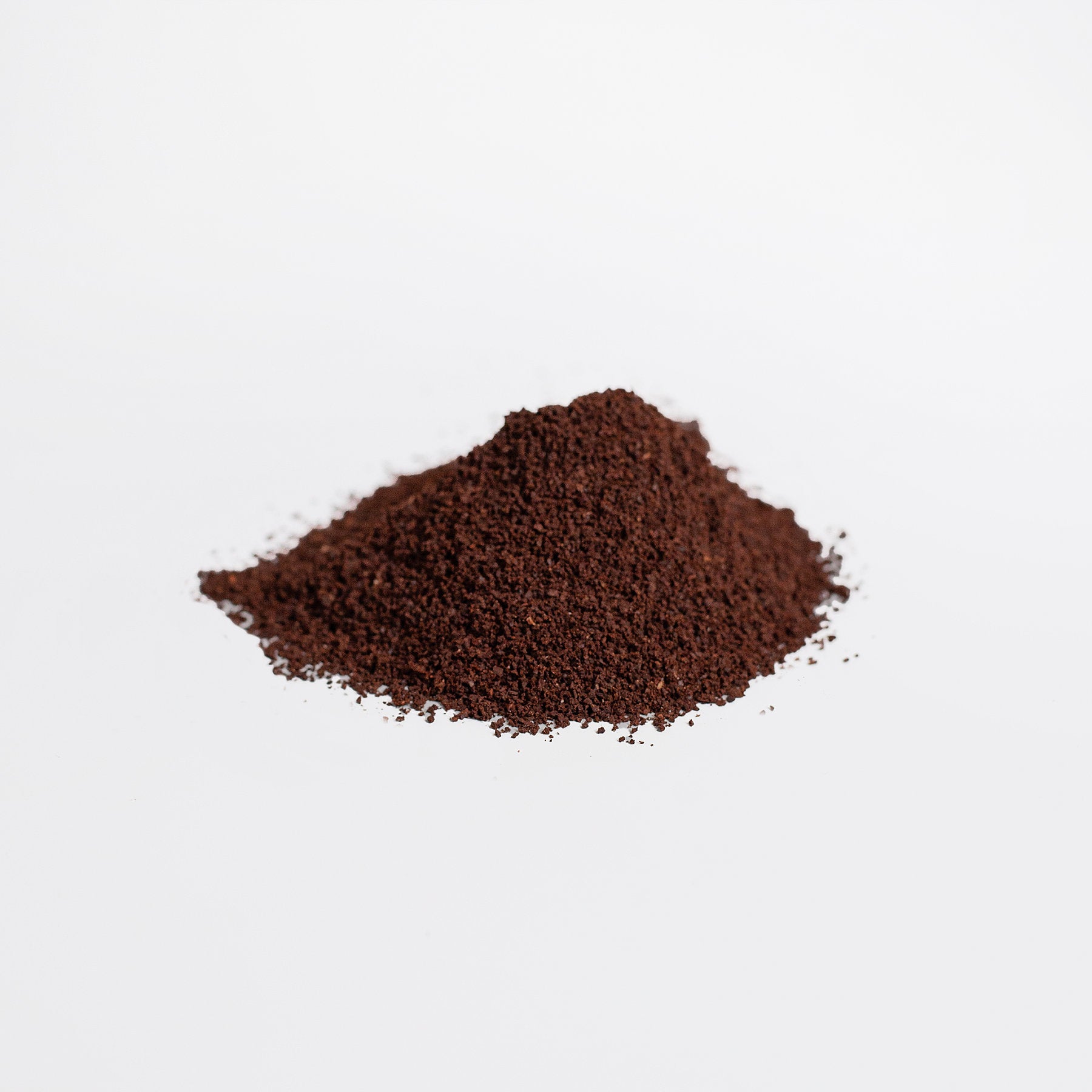 A neat mound of finely ground 111 & Co. Hemp Coffee Blend - Medium Roast 16oz, by 111 & Company, sits on a white surface. The dark brown grounds are rich and smooth in texture, with the uncluttered background highlighting the simplicity and ethical charm of the scene.