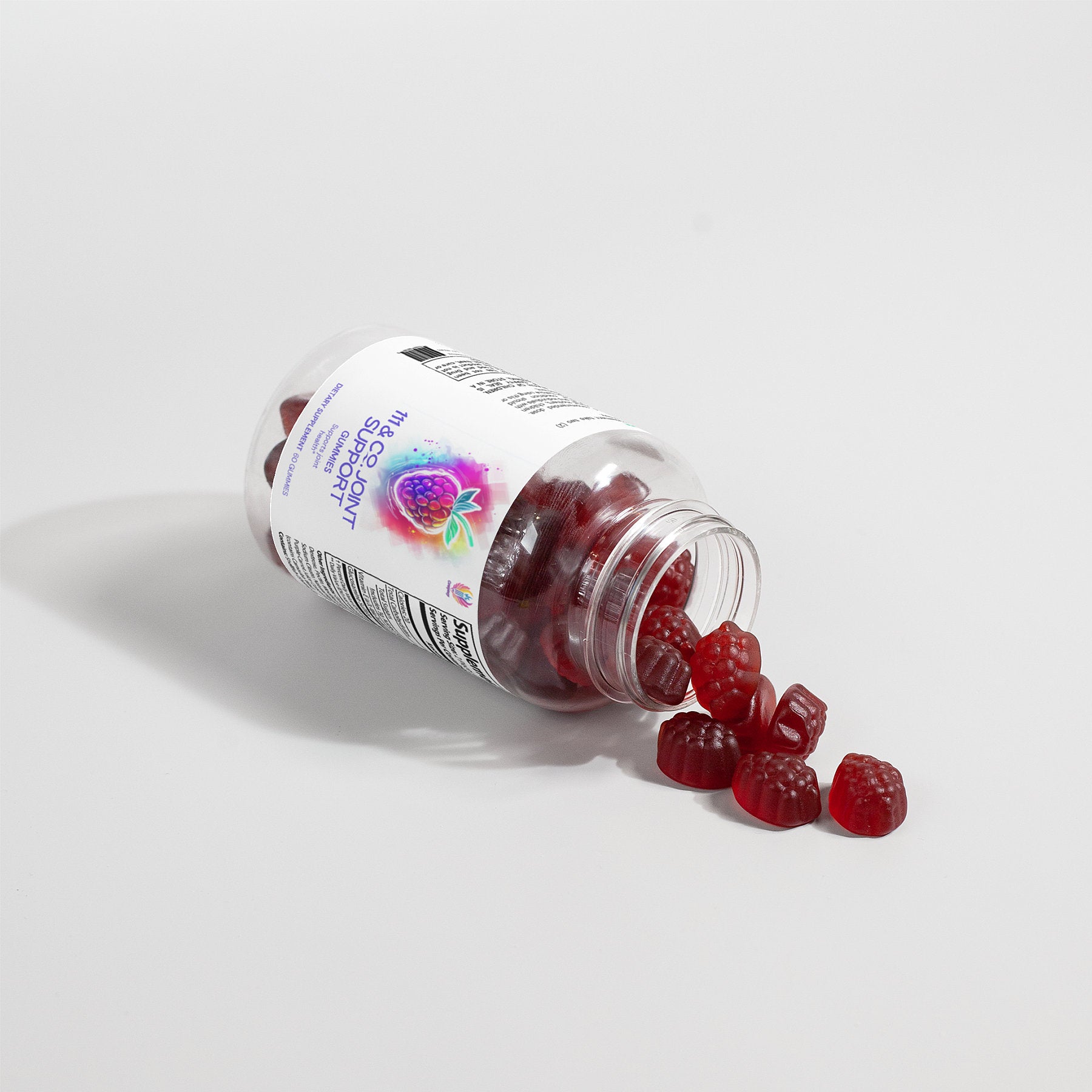 A tipped-over clear plastic bottle with a white label reveals 111 & COMPANY JOINT SUPPORT GUMMIES by 111 & Company. These red, raspberry-shaped gummies are infused with raspberry-flavored biotin for joint health, highlighted against a white background accentuating their vibrant color.