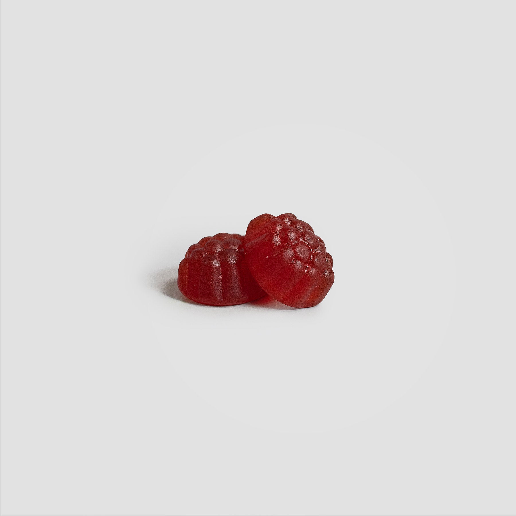 Two 111 & COMPANY JOINT SUPPORT GUMMIES by 111 & Company, shaped like raspberries and vivid red, rest on a plain light gray background. Their shiny, textured surfaces mimic real raspberries. One gummy slightly in front casts soft shadows—ideal for joint health support.