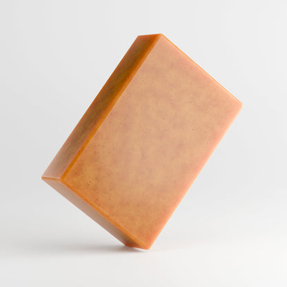 The 111 & COMPANY KOJIC ACID & TURMERIC SOAP by 111 & Company is a caramel-hued, rectangular bar with tiny dark speckles. Angled against a light gray background, it features smooth surfaces and sharp edges, offering a brightening formula for a radiant glow.
