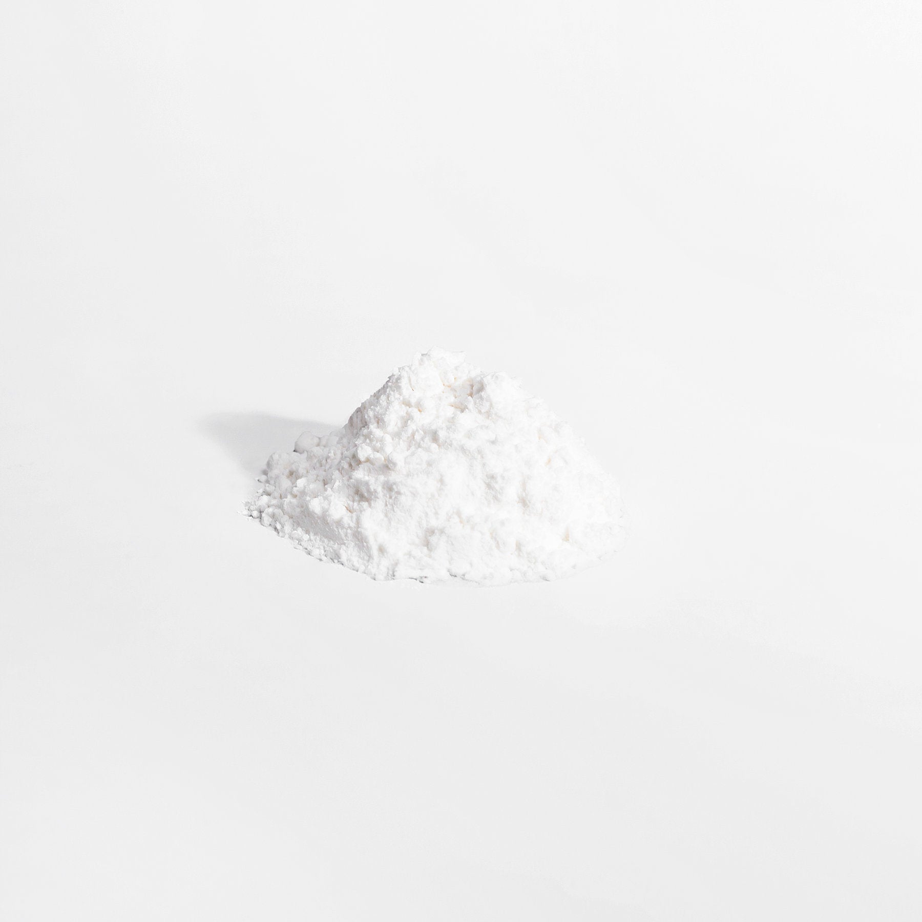 A small, slightly irregular mound of 111 & COMPANY L-GLUTAMINE POWDER from 111 & Company  sits on a plain gray background. The fine white powder, celebrated for supporting the immune system, appears soft and fluffy with subtle shadows suggesting light from the left.