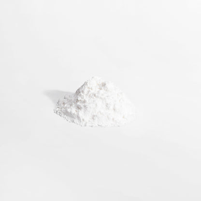 A small, slightly irregular mound of 111 & COMPANY L-GLUTAMINE POWDER from 111 & Company  sits on a plain gray background. The fine white powder, celebrated for supporting the immune system, appears soft and fluffy with subtle shadows suggesting light from the left.