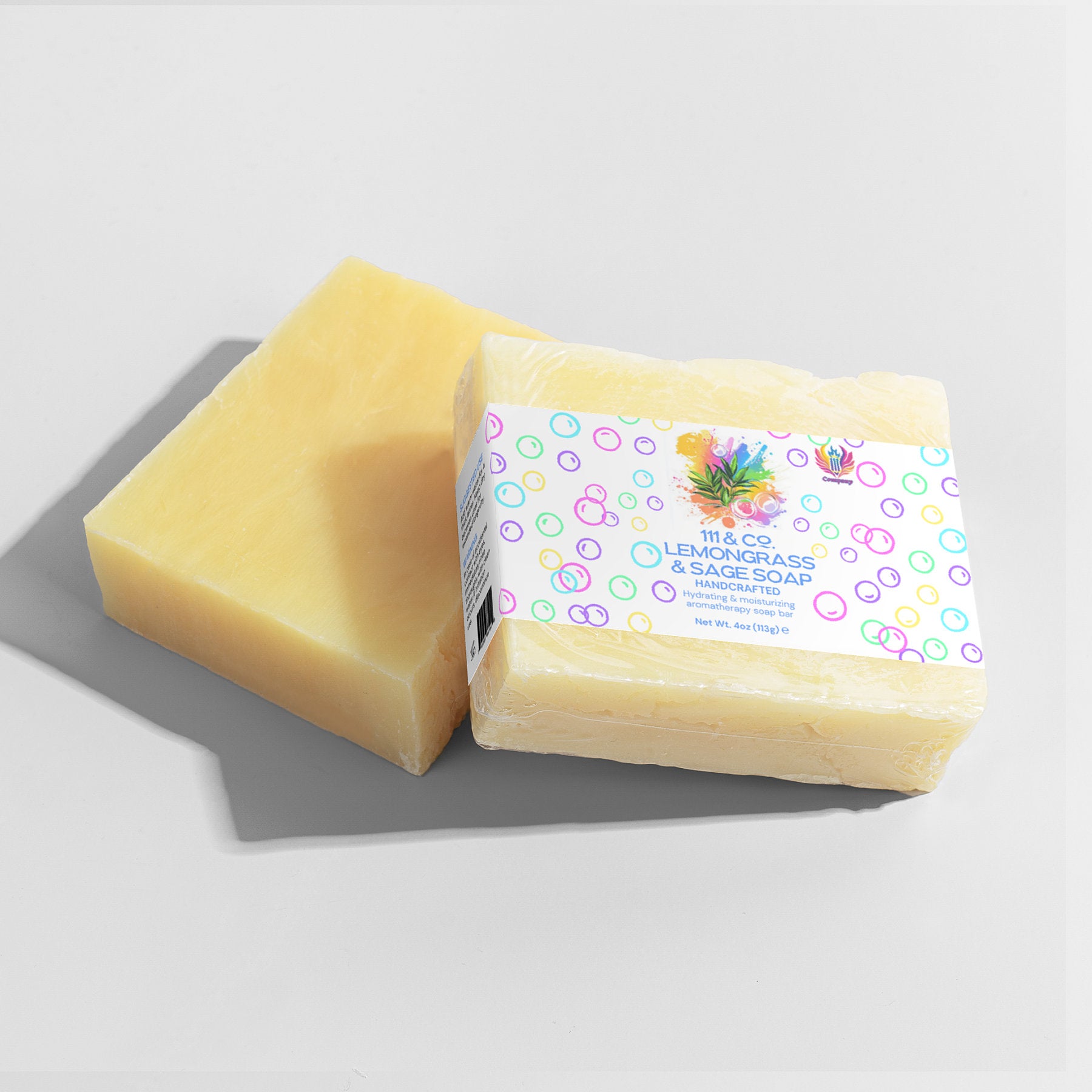 Two bars of soap lie on a light gray surface, one unwrapped with a smooth, pale yellow look ideal for sensitive skin. The other is wrapped in white paper featuring vibrant bubbles and the text:  111 & COMPANY Lemongrass & Sage Soap, Handmade. Shadows subtly cover the scene.