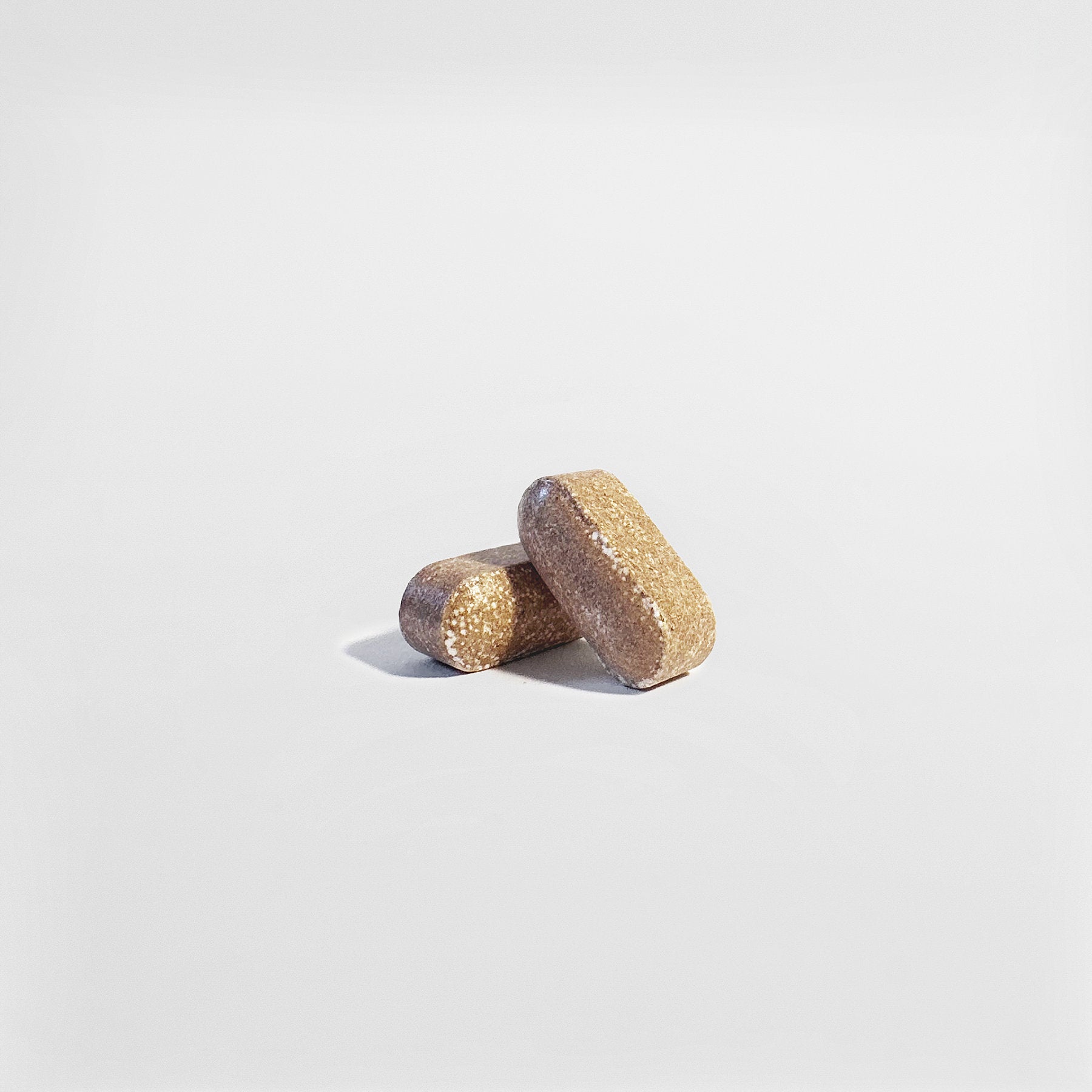 Two rectangular, brown 111 & COMPANY MENS VITALITY TABLETS by 111 & Company rest on a smooth white background. These dietary supplements reflect light slightly, emphasizing their coarse texture and granular surfaces.