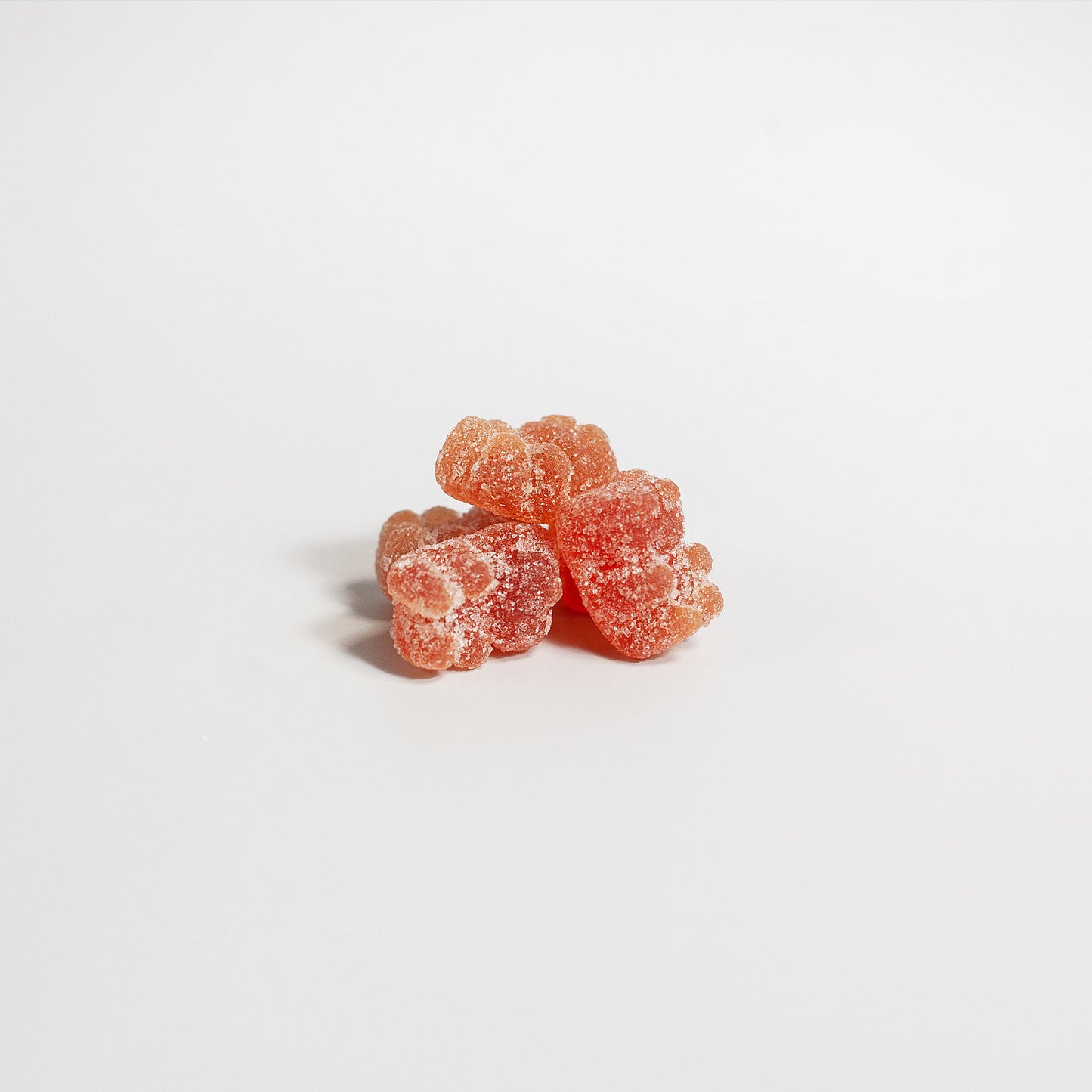 Four 111 & COMPANY MULTIVITAMIN BEAR GUMMIES for adults, lightly sugar-coated and light orange, form a loose cluster on a plain white background, revealing their chewy texture and wellness benefits.