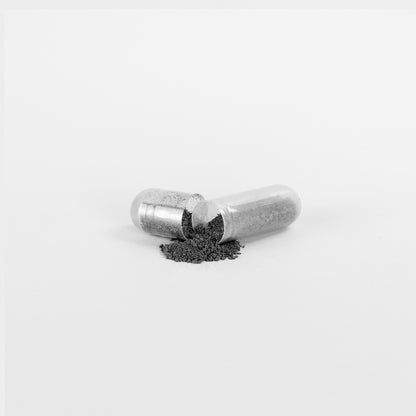 A 111 & COMPANY NATURAL GUT WELLNESS CAPSULE from 111 & Company sits open on a white surface, fine grey powder spilling out to promote digestive wellness. Capsule halves reveal granulated fulvic acid with minimalist focus on the capsule contents.