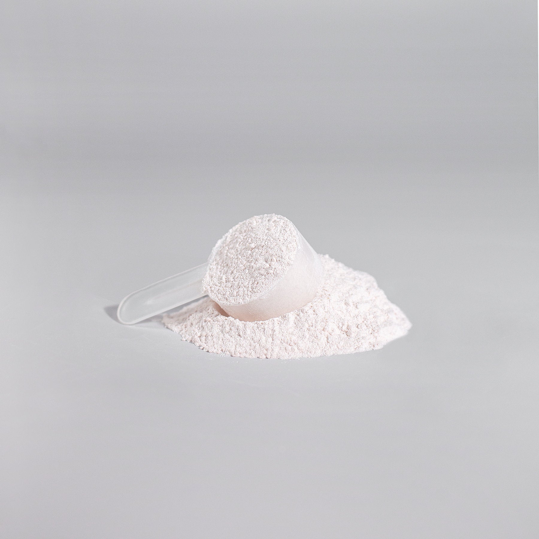 A clear plastic scoop filled with 111 & COMPANY NITRIC SHOCK PRE-WORKOUT POWDER (FRUIT PUNCH) sits on a flat gray surface, surrounded by some spilled powder forming a small mound. The smooth, light gray background enhances the scenes minimalist feel.