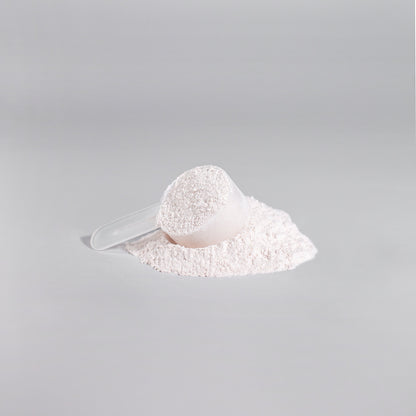 A clear plastic scoop filled with 111 & COMPANY NITRIC SHOCK PRE-WORKOUT POWDER (FRUIT PUNCH) sits on a flat gray surface, surrounded by some spilled powder forming a small mound. The smooth, light gray background enhances the scenes minimalist feel.