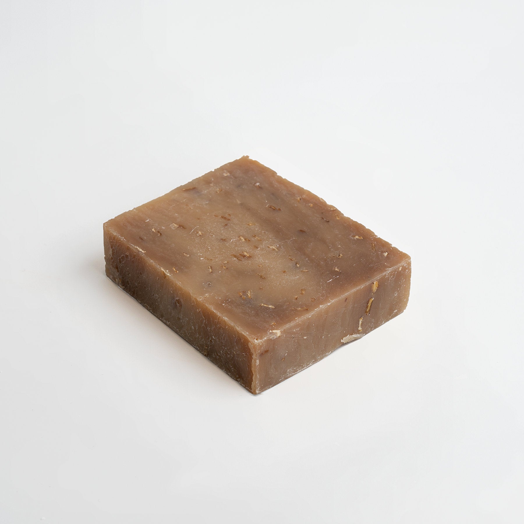 A bar of 111 & COMPANY OAT MILK HONEY SOAP in natural brown sits on a white background. Its textured surface with darker specks suggests a nourishing formula perfect for sensitive skin, while slightly rough edges add rustic charm.