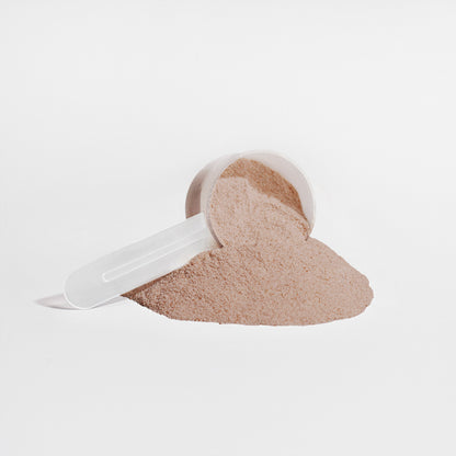 A clear scoop spills 111 & COMPANY PLANT PROTEIN (CHOCOLATE) by 111 & Company onto a white surface, forming a light brown mound. The scoops handle extends left, casting a subtle shadow against the plain white background.