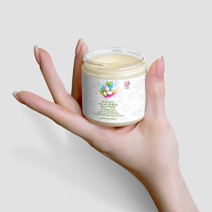 A hand with long nails holds a clear jar of  111 & COMPANY RAW SHEA BUTTER. The label, showcasing colorful fruit graphics and text, emphasizes this plant-based moisturizer. Set against a soft gray backdrop, the creamy texture inside enhances its minimalist appeal.