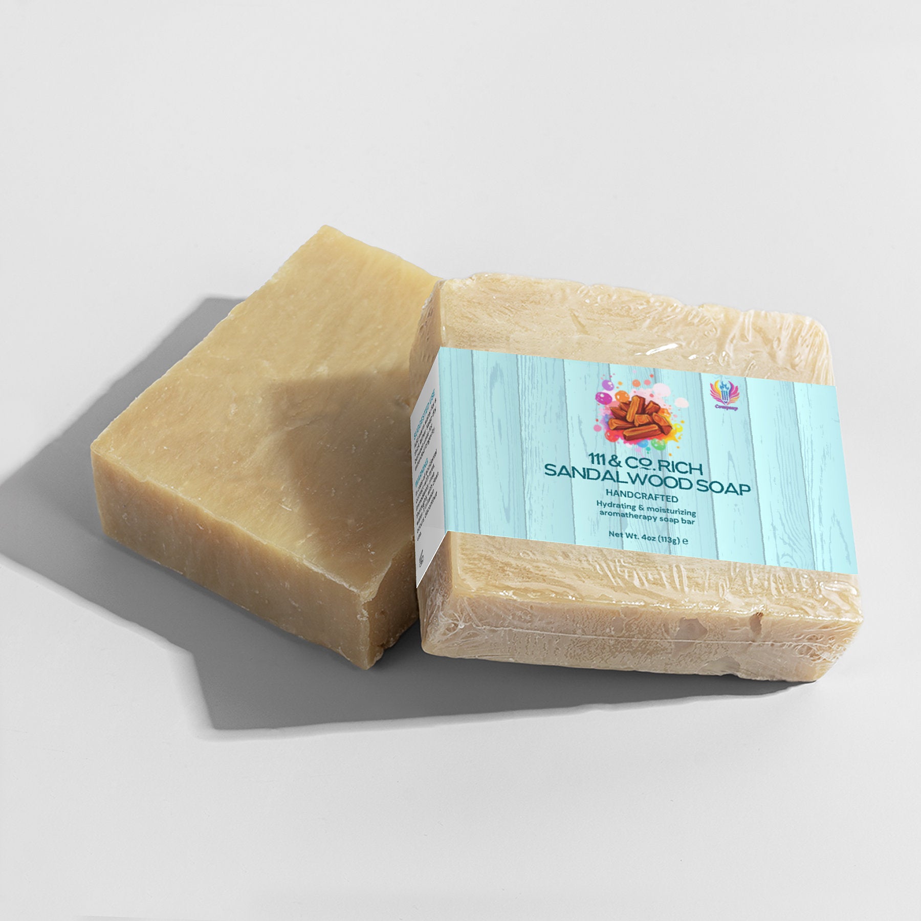 Two bars of the sand-colored, handcrafted 111 & COMPANY RICH SANDALWOOD SOAP by 111 & Company are shown. One is unwrapped, and one wrapped in plastic with a blue label featuring orange flowers and the text Moisturizing and Nourishing Rich Sandalwood Soap. Ideal for sensitive skin.