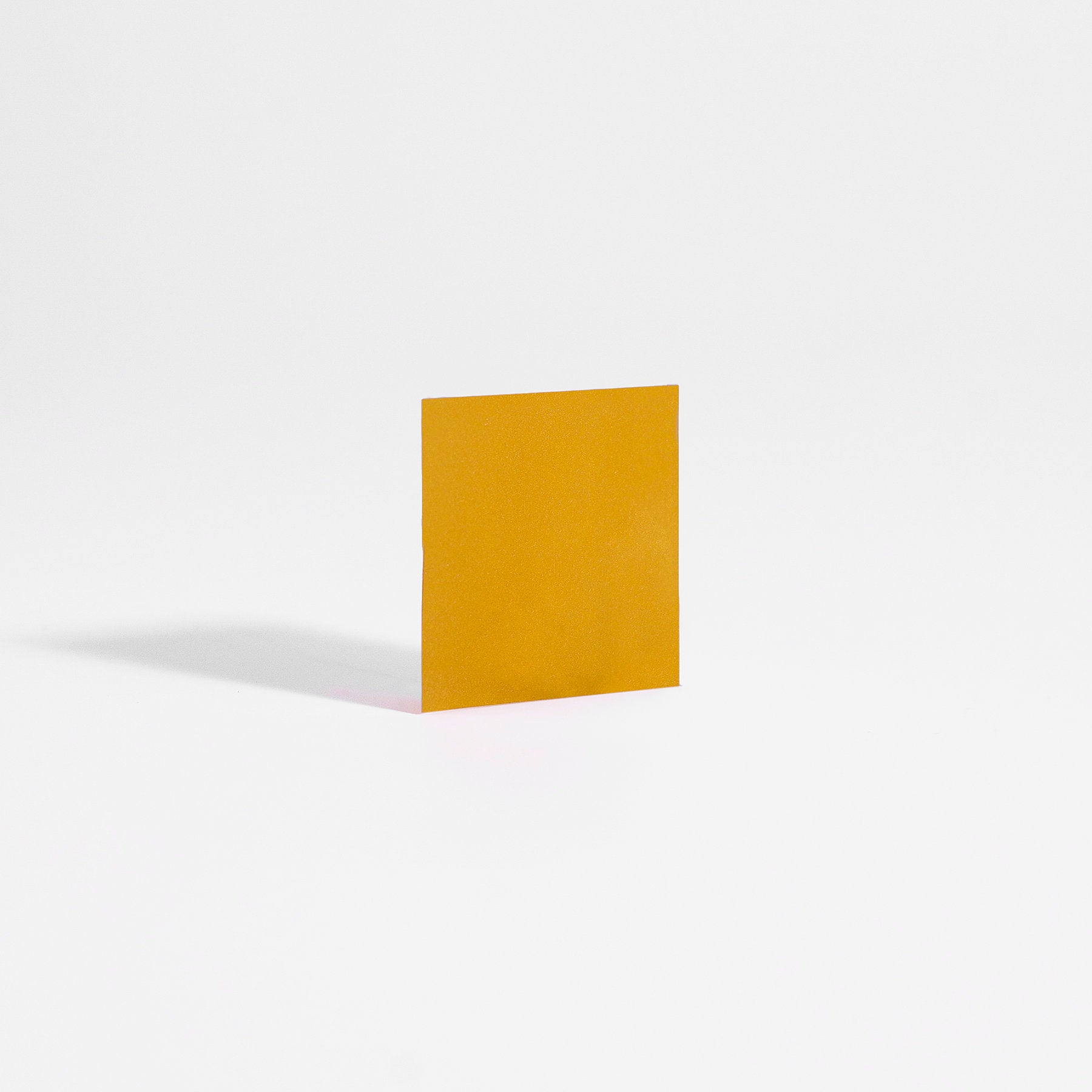 A square piece of orange paper, resembling 111 & COMPANY SLEEP STRIPS TO GO by 111 & Company, stands upright on a white background. It casts a gentle shadow leftward, reflecting the minimalist effect non-addictive sleep aids create between vivid dreams and stark reality.