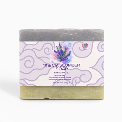 A two-tone bar of soap, dark purple atop beige, with the label 111 & COMPANY SLUMBER SOAP. It features a lavender sprig and claims to be Handcrafted, Moisturizing, with a cedar and fir forest blend, and a relaxing lavender boost. Net Wt. 4oz by 111 & Company.