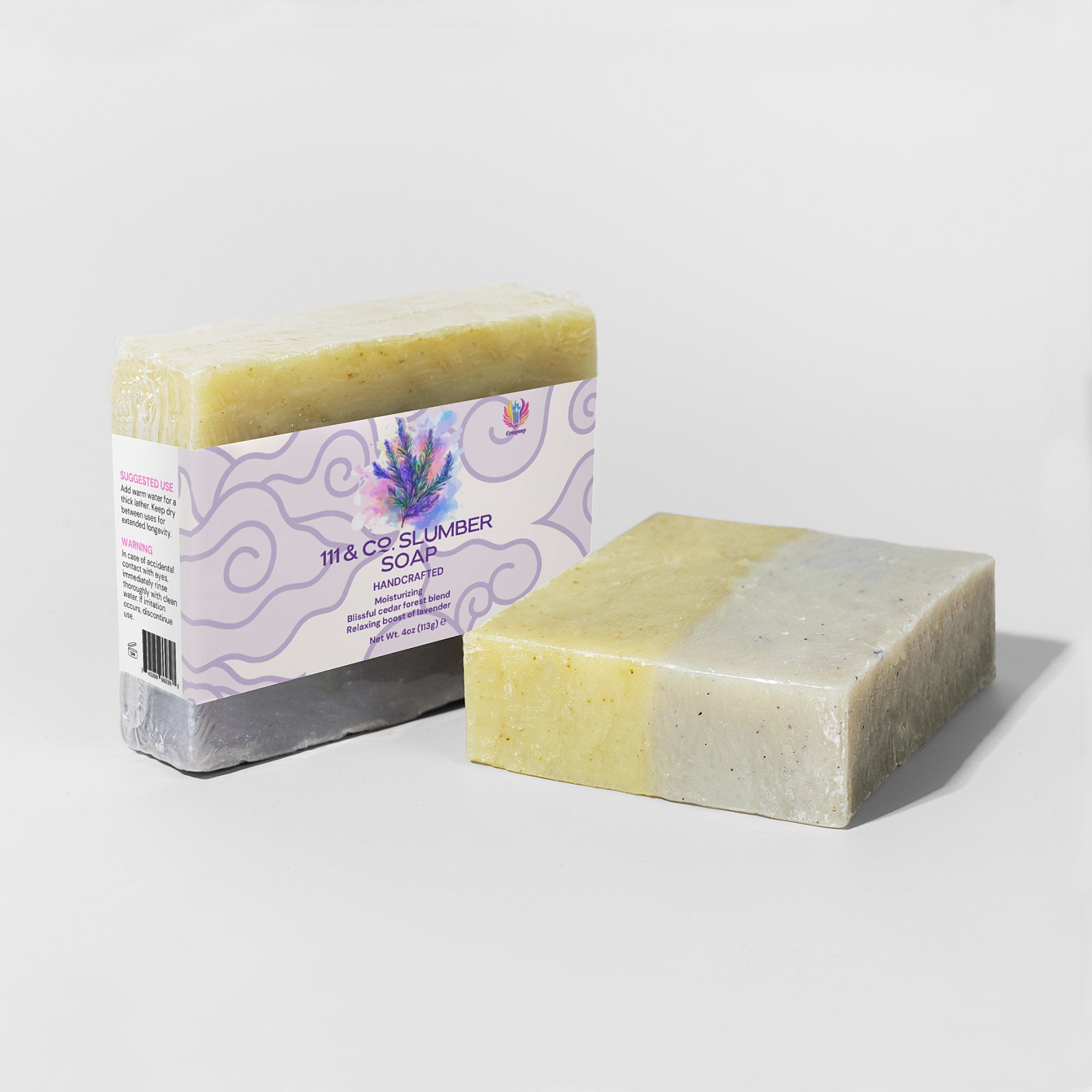 Two handcrafted soap bars are shown, one wrapped in a label reading 111 & Company Slumber Soap by 111 & Company, with lavender and fir needle imagery. The unwrapped bar reveals a marbled yellow and gray-green texture. Both rest on light gray surfaces, casting gentle shadows.