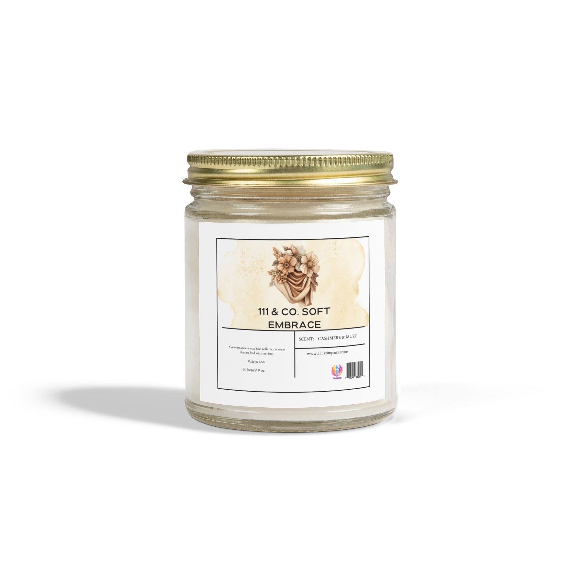 The 111 & Company Soft Embrace candle by 111 & Company comes in a clear jar with a gold metal lid, featuring a floral illustration. Its made from eco-friendly coconut apricot wax, offering vanilla, cashmere, and musk notes for 50 hours of soothing burn time against a serene white backdrop.