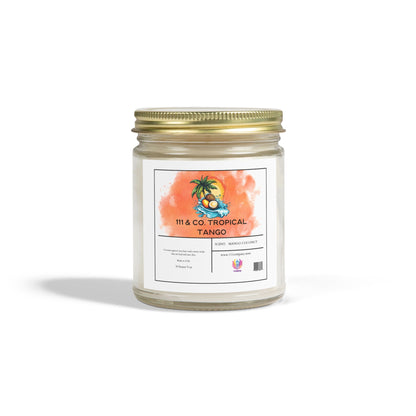 The 111 & Company Tropical Tango Candle, with a mango coconut scent, features a glass jar and gold lid. Its watercolor label showcases tropical elements like a palm tree and coconut. Crafted from eco-friendly coconut apricot wax, it sits elegantly against a plain white background.