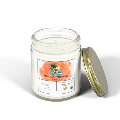 Beside it is a clear glass jar candle with a gold lid from 111 & Company, featuring a tropical palm tree and fruit scene on the label. It reads 111 & Co. Tropical Tango and Scent: Coconut Mango Candle. Made with eco-friendly coconut apricot wax for an island escape, 9 oz.