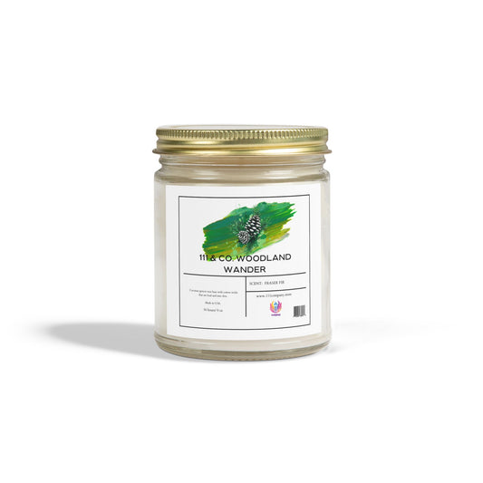 The 111 & Company Woodland Wander Fraser Fir candle in a clear jar has a gold lid, green pine cone design, and uses eco-friendly coconut apricot wax with a long-lasting burn time. It holds 9 oz and features a white background with shadow.