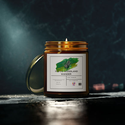 An amber jar candle labeled 111 & Company Woodland Wander Fraser Fir made from natural Coconut Apricot Wax rests on a dark surface, its lid slightly ajar. The label features a green brushstroke with a pinecone, softly spotlighted to cast gentle shadows. Brand: 111 & Company.