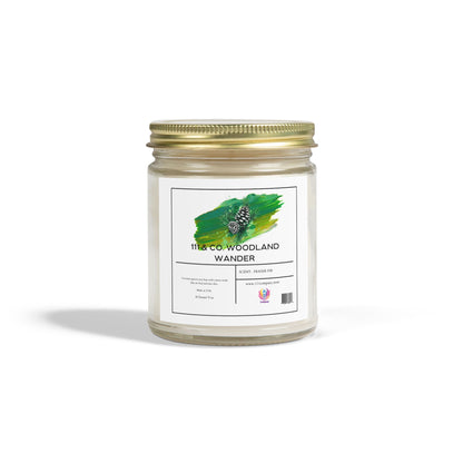 A clear glass jar with a gold lid contains the 111 & Company Woodland Wander Fraser Fir scented candle by Printify. The label has a pine cone graphic on green. Made from eco-friendly coconut apricot wax, it promises long-lasting burn time and casts a soft shadow on a white surface.