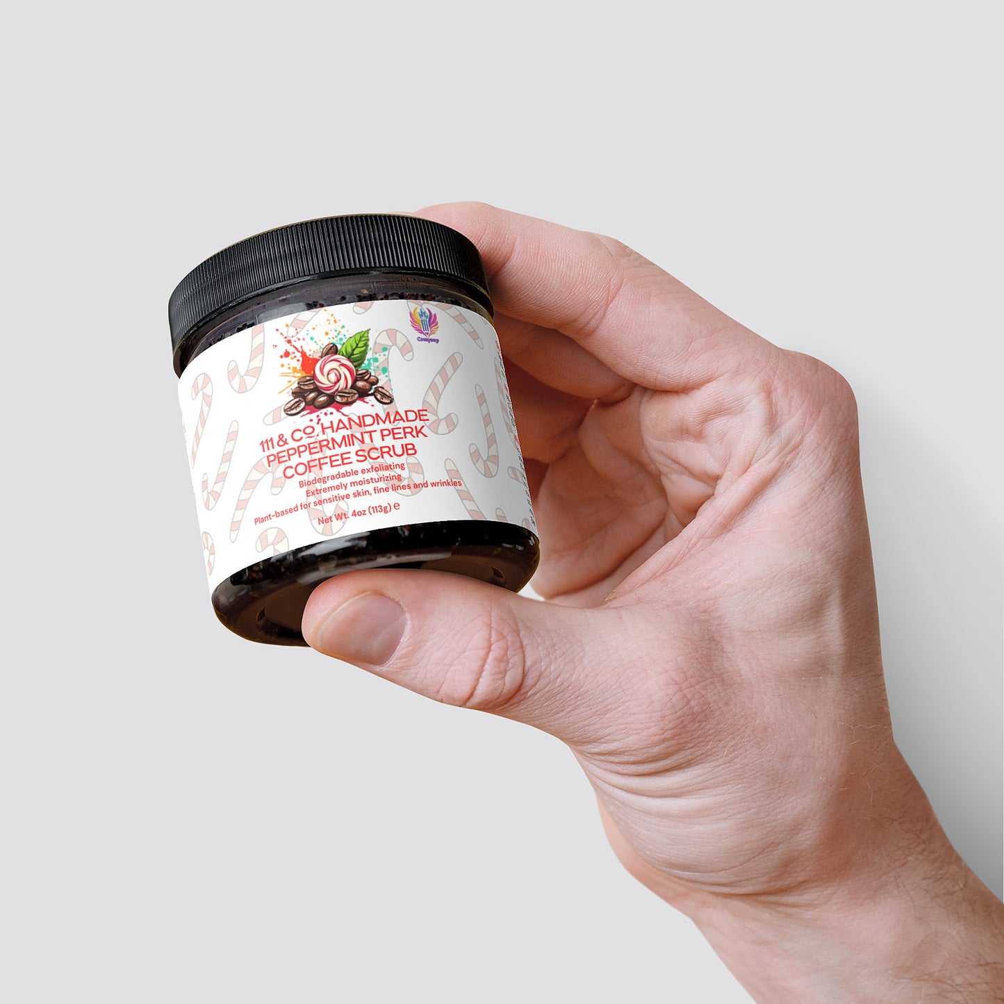 A jar of 111 & COMPANY HANDMADE PEPPERMINT PERK COFFEE SCRUB, 118g, is held in hand, offering antioxidant-rich exfoliation. The label displays peppermint swirls and candy canes on a festive design with a white backdrop. It has a black lid and is set against a plain light gray background.