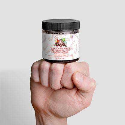 A hand holds a jar of 111 & Companys antioxidant-rich Handmade Peppermint Perk Coffee Scrub against a plain background. The jar features a white label with candy cane and peppermint designs, revealing the scrubs exfoliating texture through its clear section.