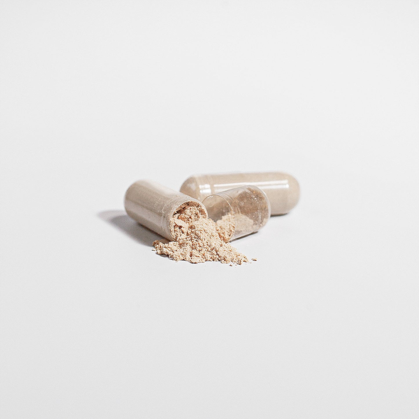 Two transparent capsules rest on a white background; one is open, spilling beige powder—a nod to its neuroprotective benefits. The other remains intact. Shadows add depth to this minimalistic scene showcasing Lions Mane Mushroom 1000 mg capsules by Retro Fitness Supplements.