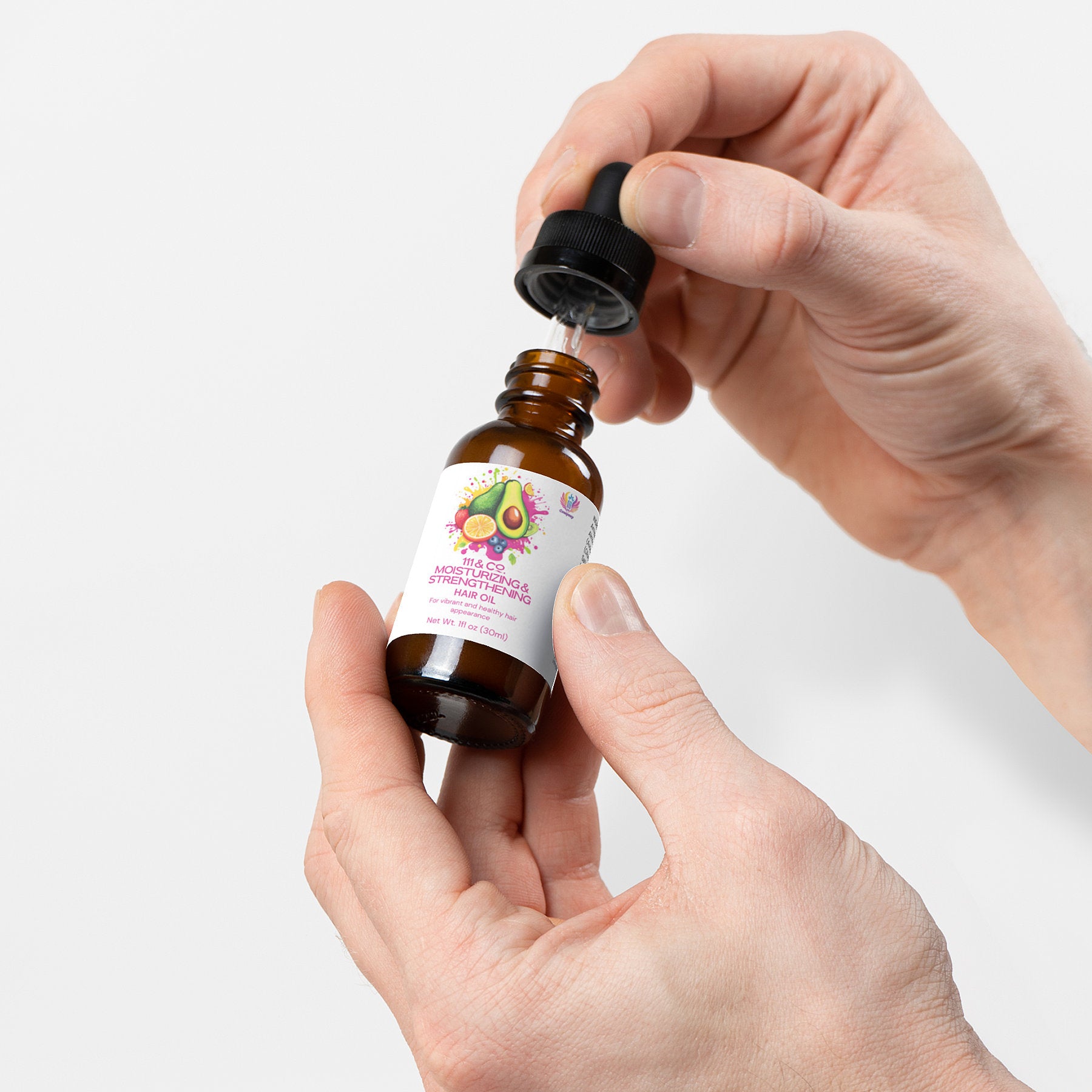 A person holds a small brown glass bottle featuring an avocado and flower design, using a dropper to extract nourishing hair oil from the 111 & COMPANY MOISTURIZING AND STRENGTHENING HAIR OIL by Retro Fitness Supplements. It promises natural strengthening, hydration, and is cruelty-free.