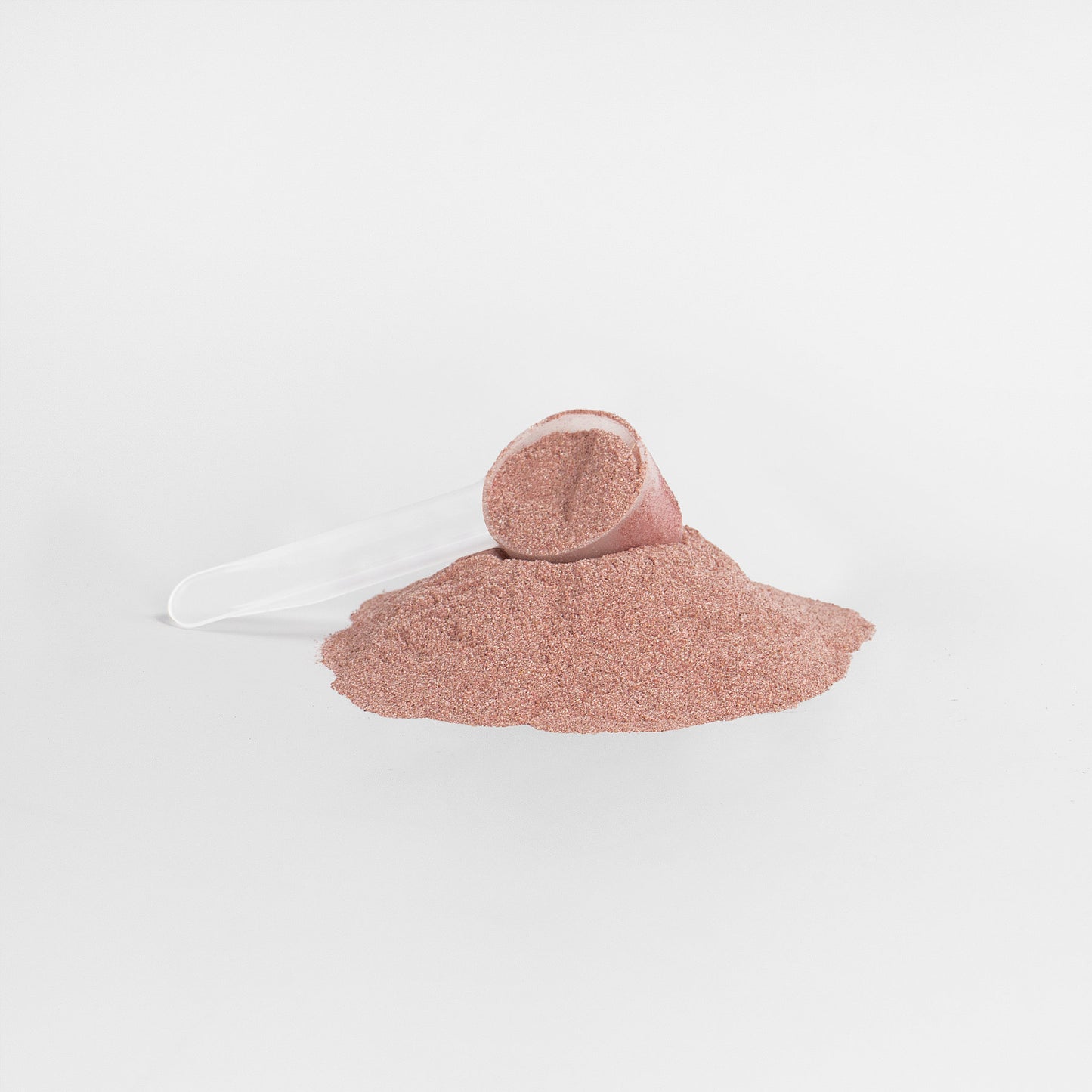 A transparent scoop rests sideways, partially buried in a small pile of fine, reddish-brown 111 & COMPANY REDS SUPERFOOD powder by Retro Fitness Supplements on a plain white background. The spilled mound suggests an inviting mix of essential nutrients and antioxidants.